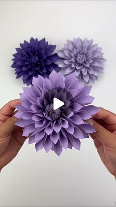 someone is holding three paper flowers in their hands, one purple and the other blue