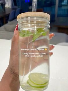 a woman holding up a mason jar filled with water and lime