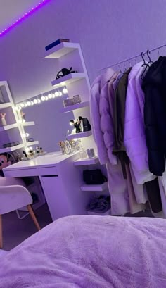 a bedroom with purple lighting and clothes hanging on the rack in front of a mirror