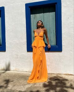 a woman in an orange dress leaning against a blue and white building with two windows