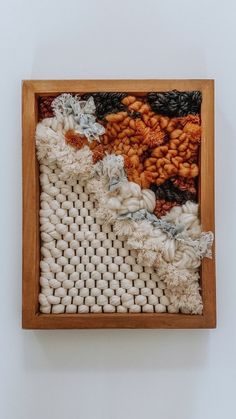 a wooden frame holding an art piece with yarn and beads on the inside, in front of a white wall