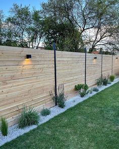 a wooden fence with two lights on it and some plants growing in the grass next to it