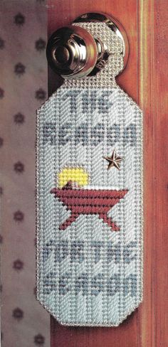 a cross - stitch door hanger with a bottle opener on it's side