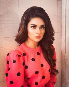 a woman with long hair wearing a red and black polka dot sweater posing for the camera