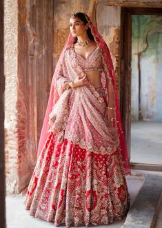 a woman in a red and gold lehenga standing on a stone floor with her arms crossed