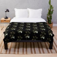 a bed with a black and red blanket on it next to a potted plant