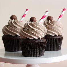 three cupcakes with chocolate frosting and candy canes on top are sitting on a plate