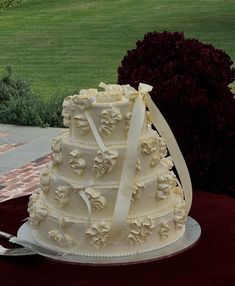 a wedding cake with white icing and bows on top sitting on a table outside