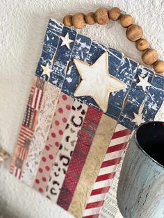 an american flag made out of scrap paper and wooden beads hangs on the wall next to a coffee cup