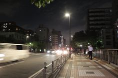 a city street at night with people walking on the sidewalk and cars driving down the road