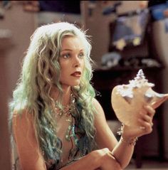 a woman with long green hair holding a seashell in her hand and looking at the camera