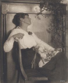 an old black and white photo of a woman sitting in a chair with her arms crossed