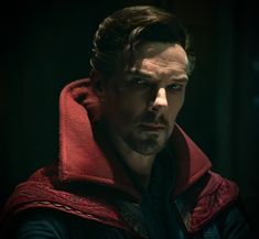 a man wearing a red hoodie in the dark with his eyes closed and one hand on his hip