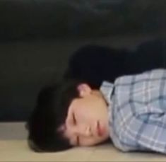 a young man laying on the floor with his head down and eyes closed, wearing a plaid shirt