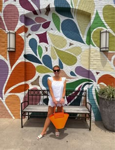 a woman sitting on a bench in front of a colorful wall