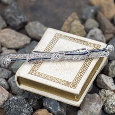 This pretty circa 1920s platinum brooch features a pierced design with engraved details and bordered with milgrain edging. The brooch is accented with seventeen (17), bead set, old European cut diamonds and eighteen (18), channel set, rectangular French cut synthetic blue sapphires. The brooch measures 65.7mm in length and 7.0mm in width. The brooch is finished with a 14K white gold pin stem and catch. Art Deco Platinum Brooches In White Gold, Art Deco White Gold Brooch In Platinum, Art Deco White Gold Platinum Brooches, Vintage Platinum Brooches With Diamond Accents, Vintage Platinum White Gold Brooches, Vintage White Gold Platinum Brooches, Vintage Platinum Brooch In White Gold, Art Deco Platinum Brooches For Anniversary, Art Deco Platinum Brooch For Formal Occasions