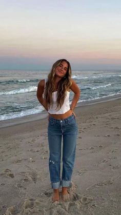 a woman standing on the beach with her hands in her pockets and looking at the camera