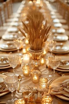 the table is set with gold plates, silverware and wheat stalks in glass vases