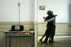 two people dancing in an empty room next to a table with a tv on it