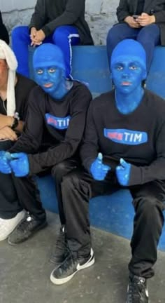 some people with blue paint on their faces sitting down and giving thumbs up to the camera