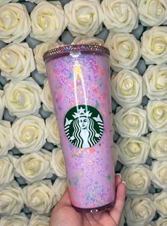 a hand holding a purple starbucks cup with sprinkles on it and white roses in the background