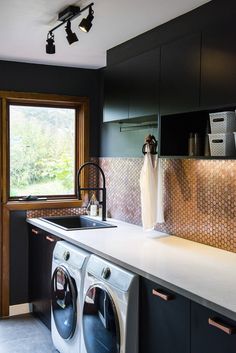 a washer and dryer in a kitchen with black cabinets, white counter tops and stainless steel backsplash