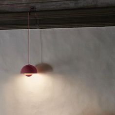 a red light hanging from the ceiling next to a white wall in a room with concrete walls