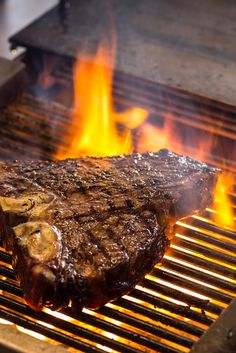 a steak is cooking on the grill with flames