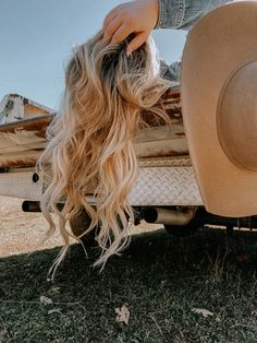 a woman with long blonde hair leaning on the back of a truck