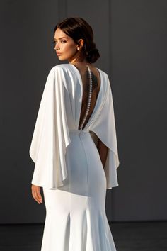 a woman in a white dress with an open back and cape on her shoulders,