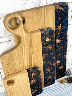 three wooden cutting boards with blue and gold designs on them, next to pine cones