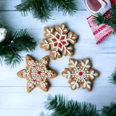 three decorated cookies sitting on top of a wooden table next to christmas decorations and pine branches