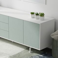 two potted plants sit on top of a white cabinet next to a gray chair