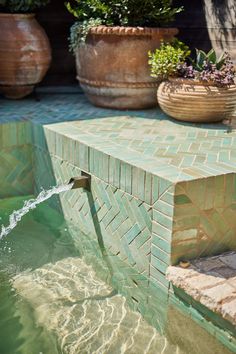 a water fountain is shown with potted plants in the background