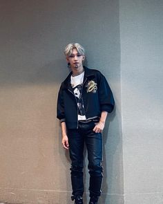 a young man standing in front of a wall wearing black leather pants and a jacket