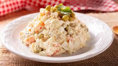 a white plate topped with chicken salad and garnished with olives next to a red checkered napkin