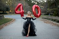 a woman in a black dress is holding two red balloons that say 40 and the number forty