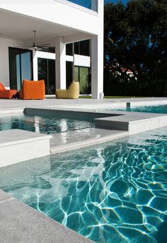 an empty swimming pool in front of a modern house with outdoor furniture and large windows