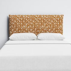 a bed with two pillows on top of it next to a white headboard and wall