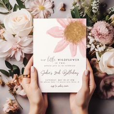 two hands holding up a pink and gold flower birthday card with the words, little wildflower on it