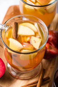 two mugs filled with apple cider and cinnamon sticks on a wooden cutting board