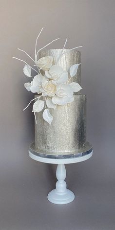 a silver and white wedding cake with flowers on top