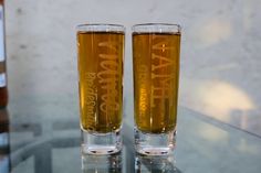 two glasses filled with liquid sitting on top of a glass table