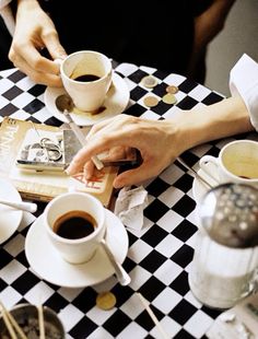 two people sitting at a table with cups of coffee and an open book on it