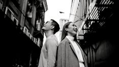 two young men standing next to each other on a city street looking up at the sky