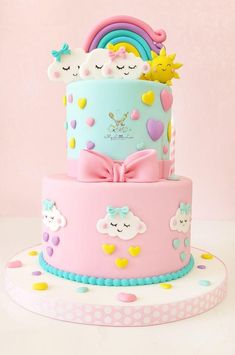 a three tiered cake decorated with rainbows, clouds and hearts on a pink background