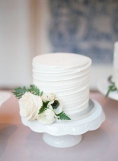 there is a white cake with flowers on the top and bottom tier, sitting on a plate