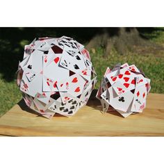 two balls made out of playing cards on top of a wooden table with grass in the background