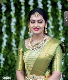 a woman in a green sari with gold jewelry on her neck and chest, smiling at the camera