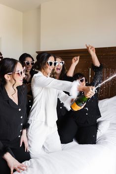 four women in black and white outfits on a bed with champagne being thrown at them